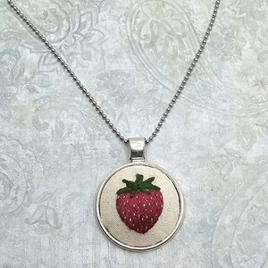 Angled close-up of a hand-embroidered strawberry pendant necklace on a silver-tone ball chain.