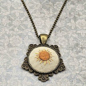 Angled view of hand embroidered sunshine necklace.